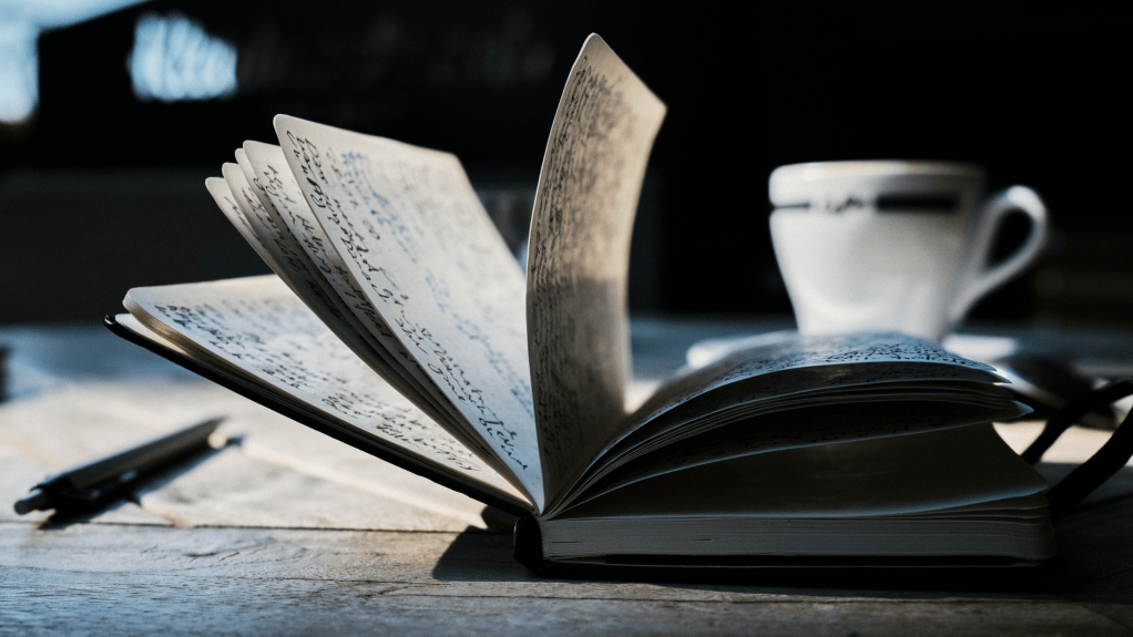 An open notebook on a table with a pen and coffee cup